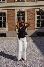Top asymétrique moulant à nouer porté par une femme, silhouette entière, cour, pantalon blanc