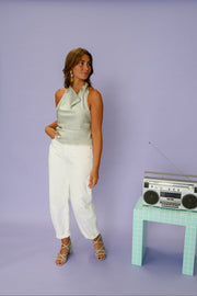 Top dentelle à col drapé porté par une femme, silhouette entière, pantalon blanc, radio, de loin