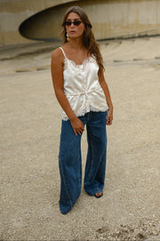 Top satiné à fines bretelles porté par une femme, silhouette entière, jean large bleu, lunettes de soleil, de loin