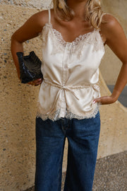 Top satiné à fines bretelles porté par une femme, vue rapprochée, pochette noire, jean bleu, taille nouée