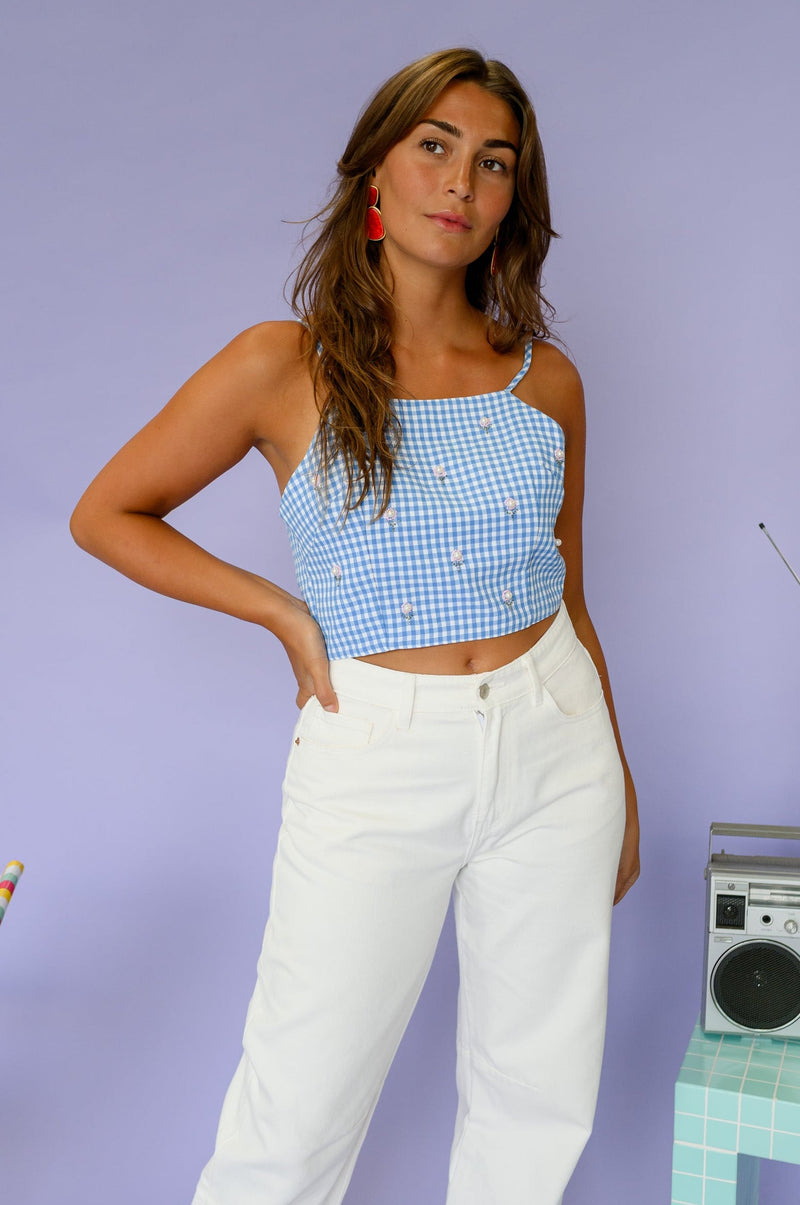 Top vichy perlé à nouer porté par une femme, vue de trois-quarts, pantalon blanc, mains sur les hanches