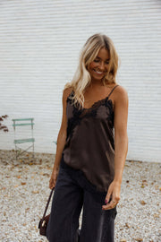 Top asymétrique en dentelle marron porté par une femme, vue de face, mur blanc, sac marron