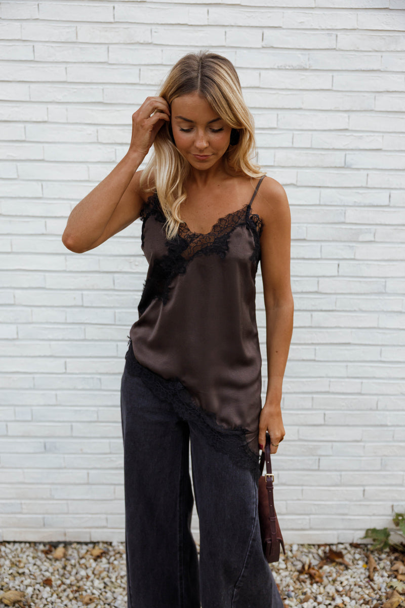 Top asymétrique en dentelle marron porté par une femme, vue de face, mur blanc, jean noir