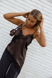 Top asymétrique en dentelle marron porté par une femme, vue rapprochée, main dans les cheveux, sac marron