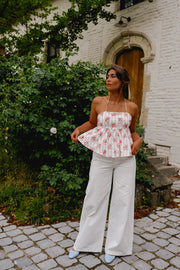Top fleuri dos ouvert noué porté par une femme, silhouette entière, pantalon blanc, verdure