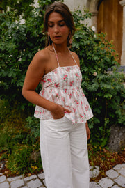 Top fleuri dos ouvert noué porté par une femme, vue de trois-quarts, pantalon blanc, buisson