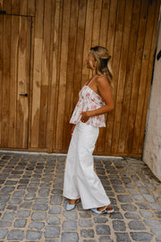 Top fleuri dos ouvert noué porté par une femme, vue de dos, pantalon blanc, porte en bois