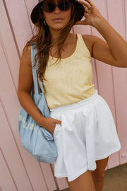 Top fluide effet lin jaune porté par une femme, vue de trois-quarts, short blanc, chapeau