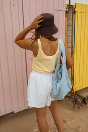 Top fluide effet lin jaune porté par une femme, silhouette entière, short blanc, chapeau