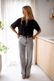 T-shirt à manches courtes noir porté par une femme, vue de face, cuisine en bois, jean gris