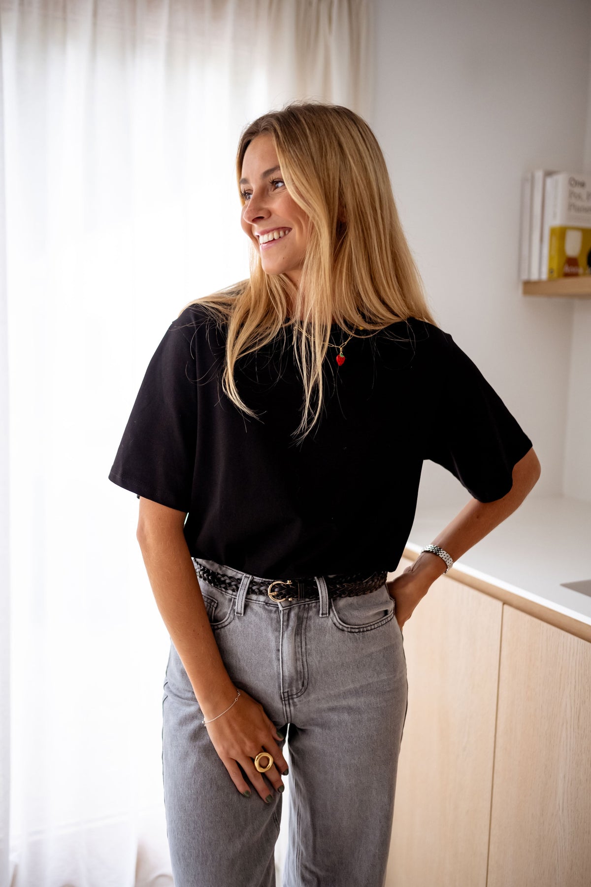 T-shirt à manches courtes noir porté par une femme, vue de face, rideaux blancs, jean gris
