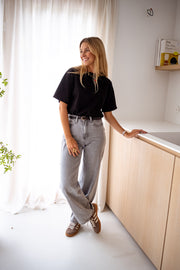 T-shirt à manches courtes noir porté par une femme, vue de face, meuble en bois, jean gris