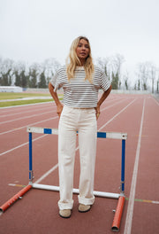 T-shirt court rayé porté par une femme, silhouette entière, haie, pantalon blanc