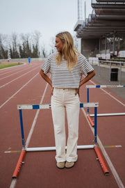 T-shirt court rayé porté par une femme, silhouette entière, haies, pantalon blanc