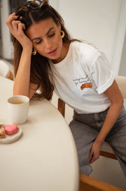 T-shirt à logo croissant blanc porté par une femme, vue rapprochée, main sur la tête, tasse