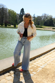 Veste à pois col montant portée par une femme, vue de trois-quarts, jean, devant un bassin