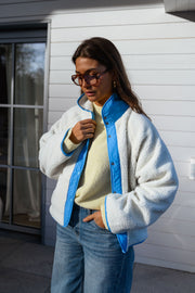 Veste réversible doublée mouton bleue portée par une femme, vue de face, côté sherpa, mur blanc