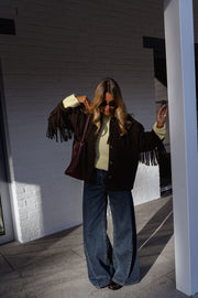 Veste à franges col revers portée par une femme, vue de face, poteau blanc, franges
