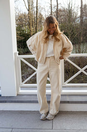 Veste en velours doublée portée par une femme, vue de face, rambarde blanche, pantalon crème