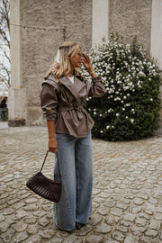 Veste effet cuir ceinturée portée par une femme, vue de profil, sac bordeaux à l'épaule