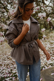 Veste effet cuir ceinturée portée par une femme, vue rapprochée, main sur le col