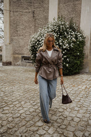 Veste effet cuir ceinturée portée par une femme, en marchant, sac bordeaux à la main, jean