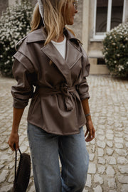 Veste effet cuir ceinturée portée par une femme, vue rapprochée, sac noir à la main
