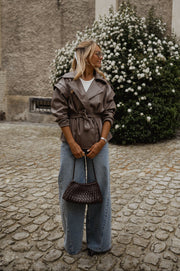 Veste effet cuir ceinturée portée par une femme, silhouette entière, sac bordeaux, jean