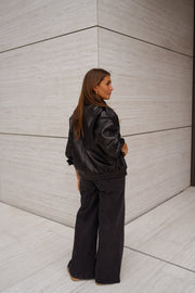Veste en simili cuir portée par une femme, vue de dos, mur beige, cheveux bruns