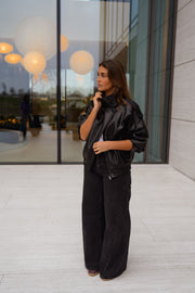 Veste en simili cuir portée par une femme, vue de face, baie vitrée, lampes