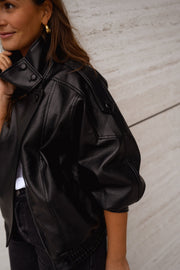 Veste en simili cuir portée par une femme, vue rapprochée, col montant, mur beige