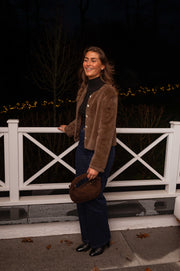Veste en fausse fourrure taupe portée par une femme, vue de face, balustrade blanche, pantalon bleu