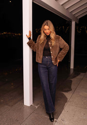 Veste en fausse fourrure taupe portée par une femme, vue de face, pantalon bleu foncé, entrée