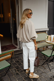 Veste zippée à manches ballon portée par une femme, vue de trois-quarts, pantalon blanc, terrasse, de dos