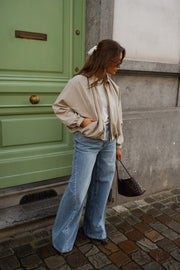 Veste zippée à manches ballon portée par une femme, vue de trois-quarts, jean, sac noir, devant une porte verte