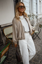 Veste zippée à manches ballon portée par une femme, vue rapprochée, lunettes de soleil, pantalon blanc
