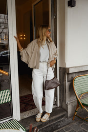 Veste zippée à manches ballon portée par une femme, silhouette entière, pantalon blanc, sac marron, devant une porte