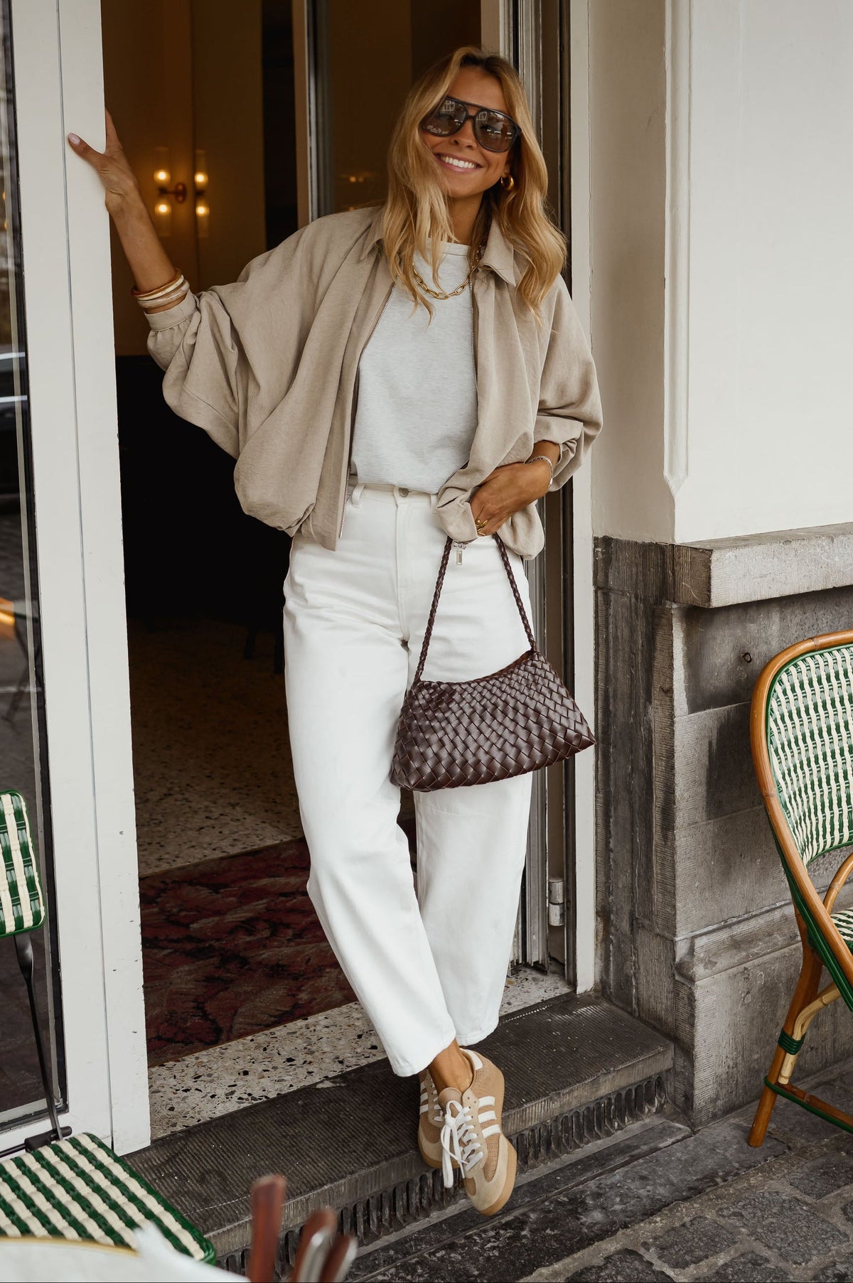 Veste zippée à manches ballon portée par une femme, silhouette entière, pantalon blanc, porte vitrée