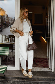 Veste zippée à manches ballon portée par une femme, silhouette entière, sac marron, pantalon blanc, terrasse