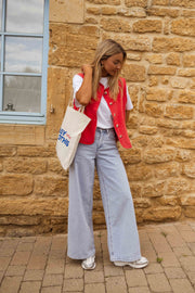 Veste sans manches boutonnée rouge portée par une femme, vue de face, mur en pierre, fenêtre
