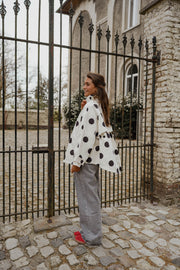 Veste souple à pois portée par une femme, silhouette entière, devant un portail, pantalon gris