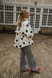 Veste souple à pois portée par une femme, vue de dos, chaussures rouges, pantalon gris
