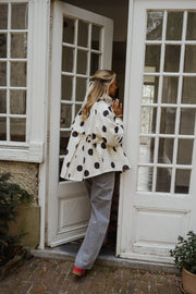Veste souple à pois portée par une femme, silhouette entière, devant une porte vitrée, chaussures rouges
