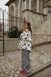 Veste souple à pois portée par une femme, vue de profil, devant un portail