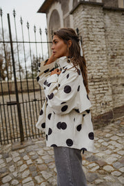 Veste souple à pois portée par une femme, vue de trois-quarts, devant un portail