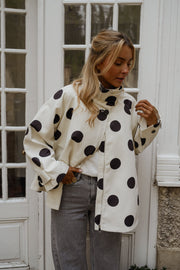 Veste souple à pois portée par une femme, silhouette entière, devant une porte vitrée, pantalon gris