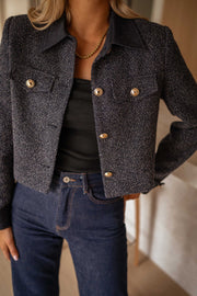 Veste en tweed à poches bleue portée par une femme, vue rapprochée, boutons dorés, haut noir