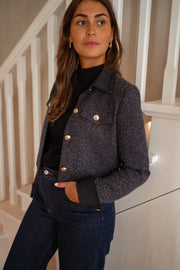 Veste en tweed à poches bleue portée par une femme, vue de trois-quarts, escalier, haut noir