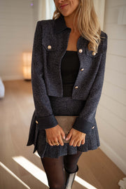 Veste en tweed à poches bleue portée par une femme, vue rapprochée, jupe plissée grise, sac
