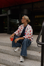 Veste imprimée à boutons-pression portée par une femme, assise, sur des marches, gobelet à la main